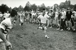 Fairfield University students in shorts and caps cheer on their fellow students who are racing across the field